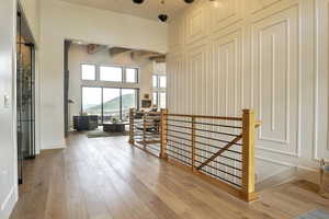 Corridor with an upstairs landing, beam ceiling, and light wood-type flooring