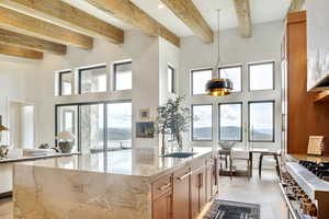 Kitchen with a kitchen island with sink, light stone counters, decorative light fixtures, beam ceiling, and high end range