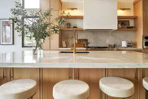 Bar area featuring light stone countertops, open shelves, stainless steel oven, and brown cabinets