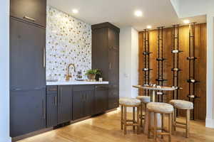 Indoor wet bar with light wood-style floors, light stone counters, recessed lighting, and modern cabinets