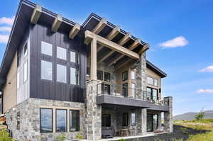 Back of house with stone siding, board and batten siding, a balcony, a patio area, and a mountain view