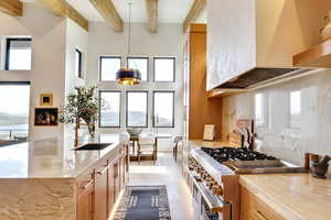 Kitchen with custom range hood, backsplash, double oven range, light stone countertops, and beamed ceiling