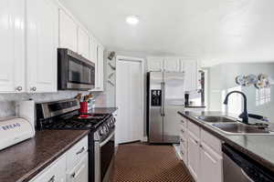 Kitchen with stainless steel appliances, dark countertops, white cabinetry, and tasteful backsplash