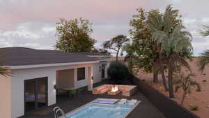 Back of property at dusk with stucco siding and a pool with connected hot tub
