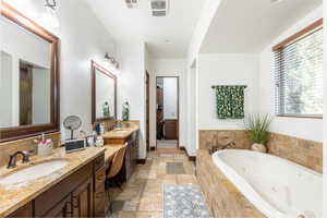 Bathroom featuring stone tile flooring, double vanity, and a whirlpool tub