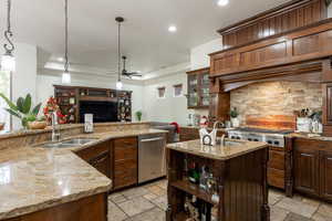 Kitchen with an island with sink, hanging light fixtures, light stone counters, and recessed lighting