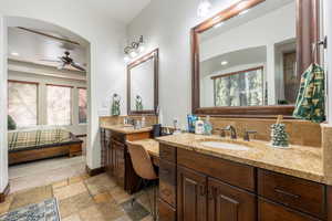 Ensuite bathroom featuring double vanity, stone tile flooring, plenty of natural light, recessed lighting, and ceiling fan
