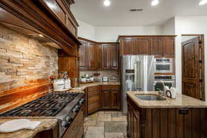 Kitchen featuring tasteful backsplash, stainless steel appliances, custom exhaust hood, light stone countertops, and dark brown cabinets