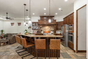 Kitchen with pendant lighting, glass insert cabinets, a breakfast bar, light stone counters, and recessed lighting