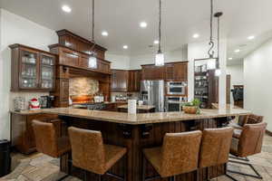 Kitchen featuring decorative backsplash, stone tile flooring, glass insert cabinets, stainless steel appliances, and recessed lighting