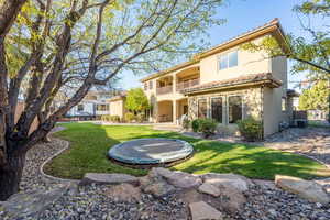 Back of property featuring a balcony, a trampoline, a patio area, stucco siding, and a tiled roof