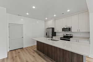 Kitchen with appliances with stainless steel finishes, an island with sink, light stone counters, light wood-style floors, and recessed lighting