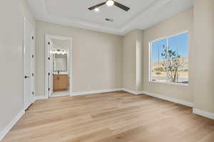 Unfurnished bedroom with light wood-style flooring, a raised ceiling, ceiling fan, recessed lighting, and ensuite bath