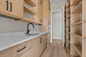 Kitchen featuring light brown cabinetry, open shelves, light wood-style flooring, light stone countertops, and oven