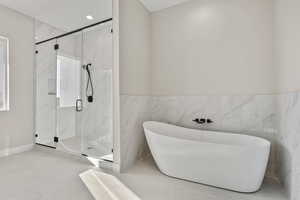 Bathroom with a freestanding tub, a marble finish shower, tile walls, recessed lighting, and a wainscoted wall