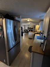 Kitchen featuring freestanding refrigerator, white cabinetry, a textured ceiling, light wood-style floors, and open floor plan