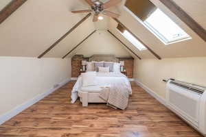 Bedroom featuring a skylight, light wood-type flooring, lofted ceiling, a ceiling fan, and a wall unit AC
