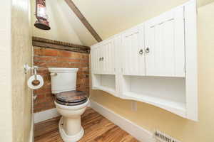 Half bath featuring brick wall, wood finished floors, vaulted ceiling, and a textured wall
