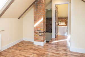 Additional living space with vaulted ceiling, wood finished floors, a skylight, and brick wall