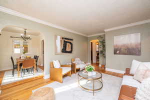 Living area featuring a chandelier, arched walkways, wood finished floors, crown molding, and a textured ceiling