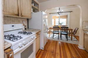 Kitchen with white appliances, crown molding, light countertops, arched walkways, and decorative backsplash