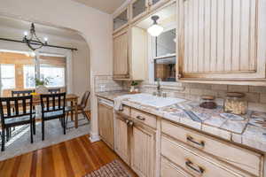 Kitchen with tile countertops, ornamental molding, glass insert cabinets, light wood finished floors, and a chandelier