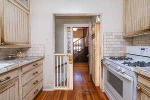 Kitchen featuring tile counters, backsplash, white range with gas cooktop, a textured wall, and light brown cabinetry