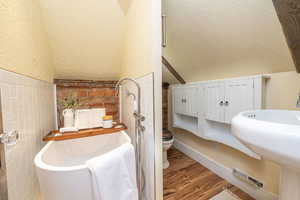 Full bathroom featuring a textured ceiling, light wood-type flooring, lofted ceiling, a textured wall, and a soaking tub