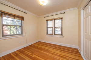 Empty room with a textured ceiling, wood-type flooring, crown molding, and plenty of natural light