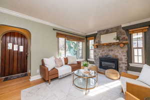 Living area featuring arched walkways, crown molding, a textured wall, wood finished floors, and a fireplace