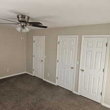 Unfurnished bedroom with dark carpet and a ceiling fan
