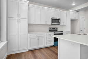 Kitchen with stainless steel appliances, light stone counters, white cabinets, and dark wood-type flooring