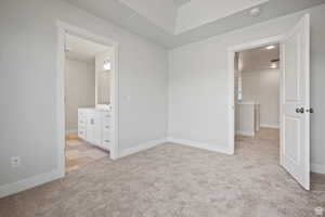 Unfurnished bedroom with light colored carpet and connected bathroom
