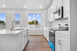 Kitchen featuring appliances with stainless steel finishes, white cabinets, light stone counters, light wood-type flooring, and an island with sink