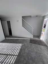 Unfurnished living room with stairs and carpet floors