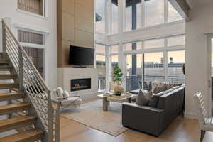Living area with a glass covered fireplace, light wood-style flooring, a high ceiling, and stairs