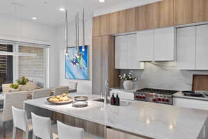 Kitchen with modern cabinets, white cabinets, light stone counters, an island with sink, and recessed lighting