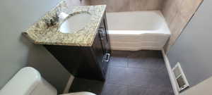 Bathroom with vanity, a tub to relax in, and dark tile patterned flooring