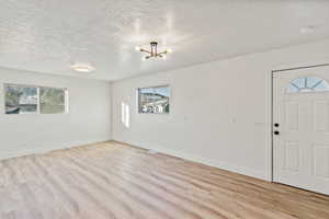 Entrance foyer featuring a textured ceiling, light wood-type flooring, and a chandelier