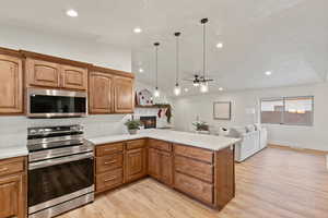 Kitchen with stainless steel appliances, brown cabinets, light countertops, a peninsula, and hanging light fixtures