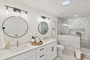 Full bath featuring a marble finish shower, double vanity, light marble finish flooring, a textured ceiling, and recessed lighting