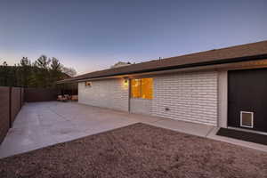 Back of property at dusk with brick siding, a fenced backyard, and a patio area