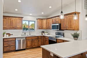 Kitchen featuring brown cabinets, a peninsula, appliances with stainless steel finishes, decorative light fixtures, and recessed lighting