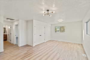 Unfurnished bedroom featuring a textured ceiling, light wood-type flooring, two closets, a chandelier, and ensuite bath