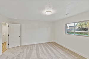 Empty room featuring a textured ceiling and light colored carpet