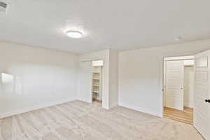 Unfurnished bedroom featuring a textured ceiling, light colored carpet, and a spacious closet