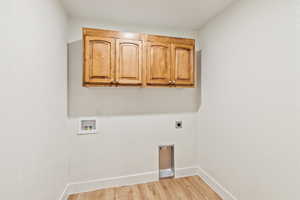 Laundry area with cabinet space, light wood-style flooring, hookup for an electric dryer, and hookup for a washing machine