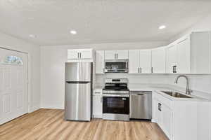 Kitchen featuring stainless steel appliances, white cabinets, recessed lighting, light wood finished floors, and a textured ceiling