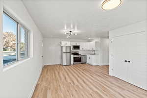 Kitchen with white cabinets, appliances with stainless steel finishes, light countertops, light wood-type flooring, and a textured ceiling
