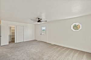 Unfurnished bedroom with a spacious closet, light carpet, a textured ceiling, and a ceiling fan